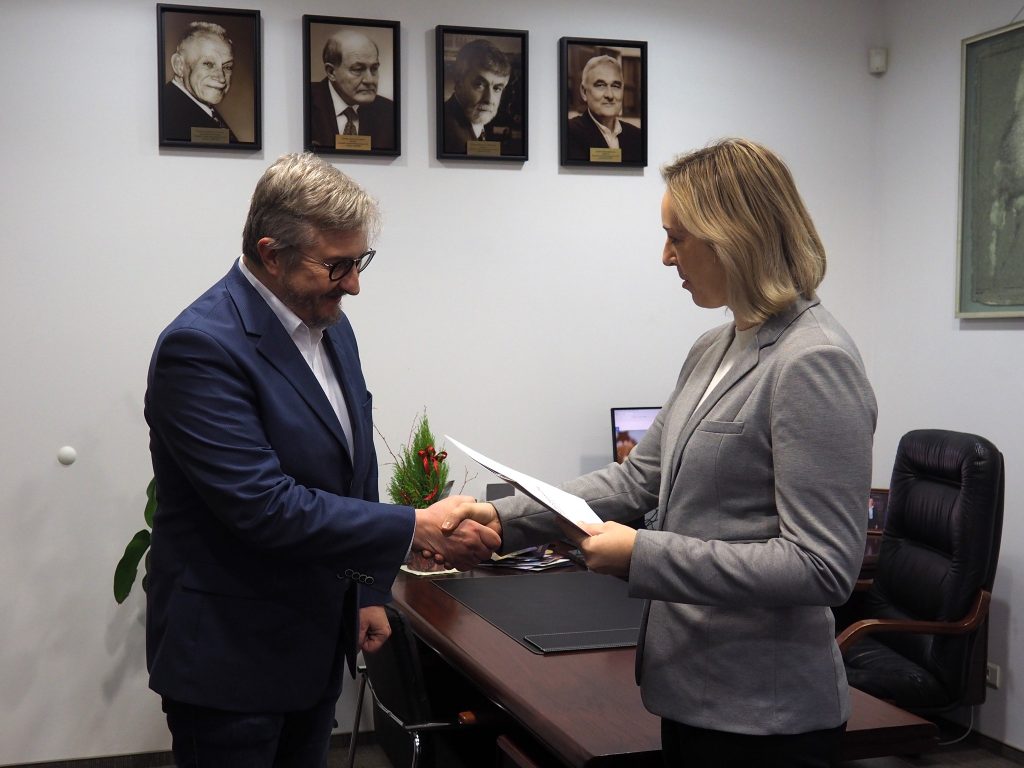 Gabinet Dyrektora ICHB PAN, w tyle portrety dotychczasowych Dyrektorów ICHB PAN zawieszone na ścianie. Dr hab. Luiza Luiza Handschuh ściska dłoń Roberta Pękala.